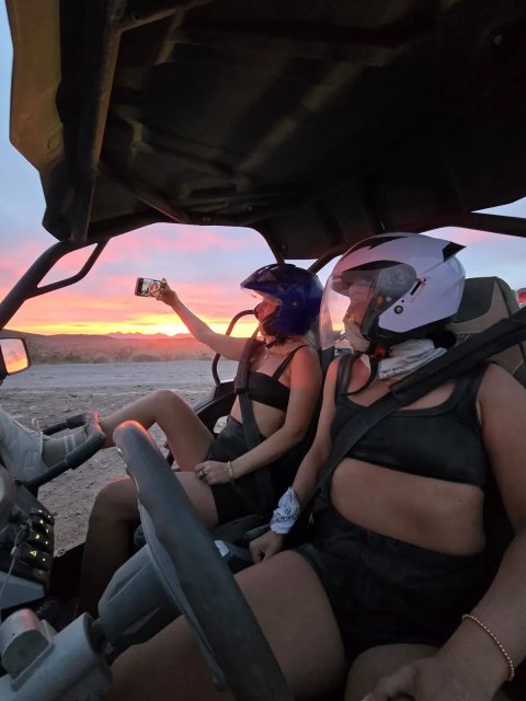 Two riders taking a selfie inside their sand buggy at sunset